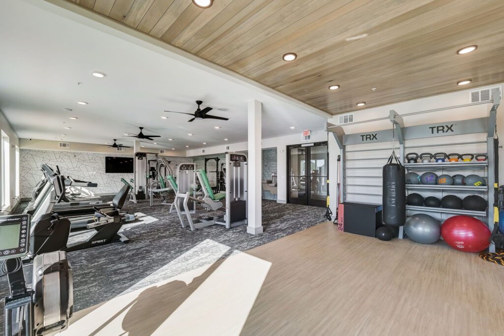 Modern gym with treadmills, weight machines, punching bag, TRX equipment, and exercise balls, featuring wooden ceiling and bright lighting.