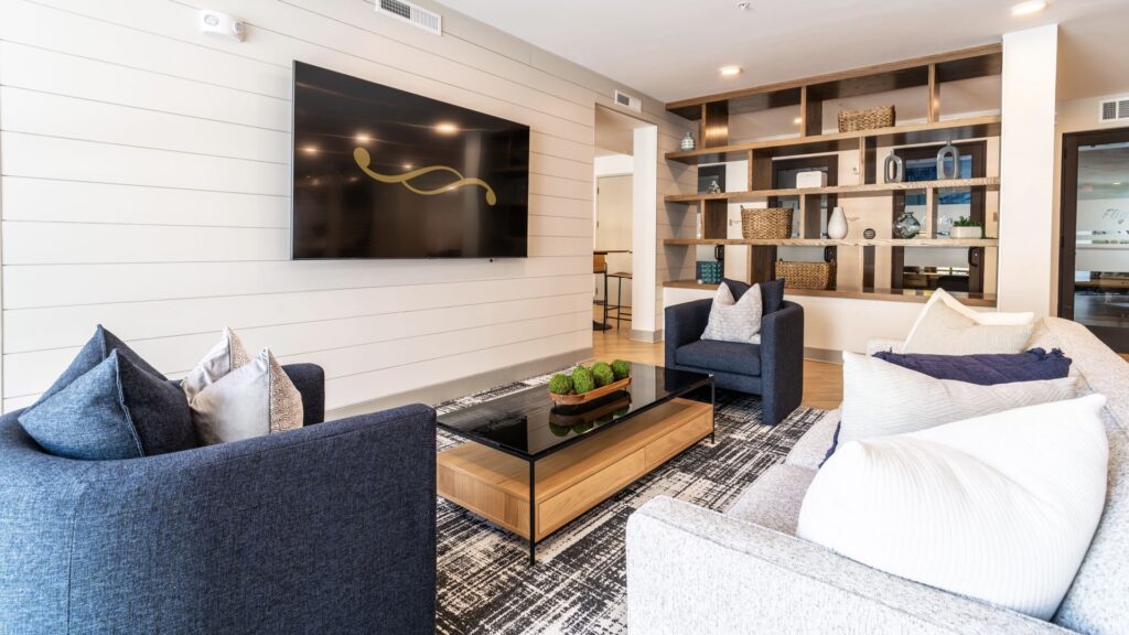 Modern living room with two sofas and armchairs, a large wall-mounted TV, wooden coffee table, and built-in shelves with decor.