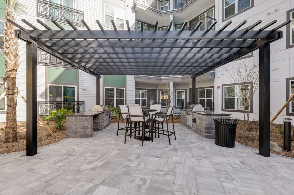 Outdoor patio area with a metal pergola, tall chairs, and a built-in grill set within a residential building courtyard.