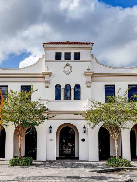 Two-story white building with decorative architectural features, arched entrance, and two trees in front.